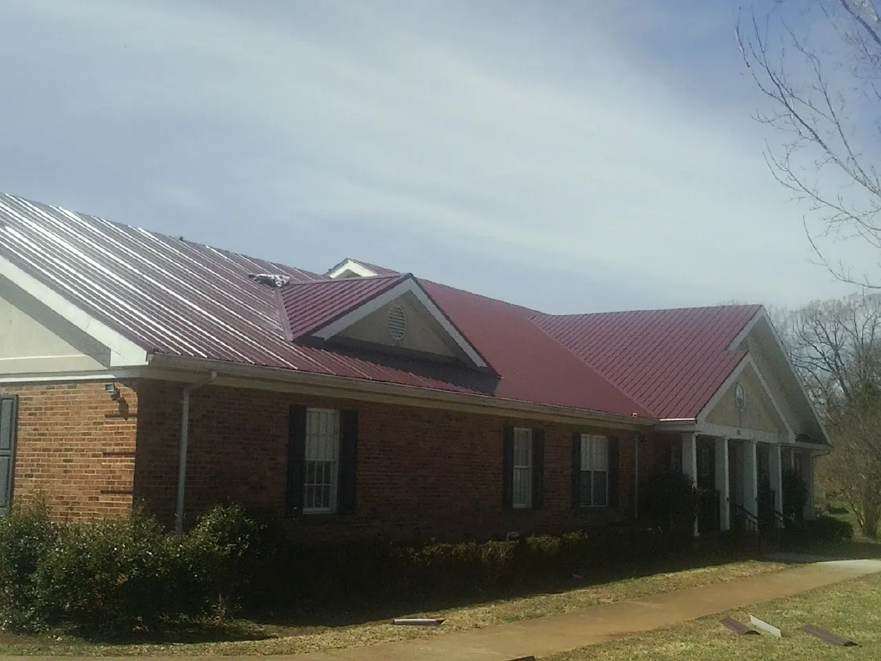 Red metal roof with gabled entries on a long brick building, from a Hail Damage Roof Repair job in Millville