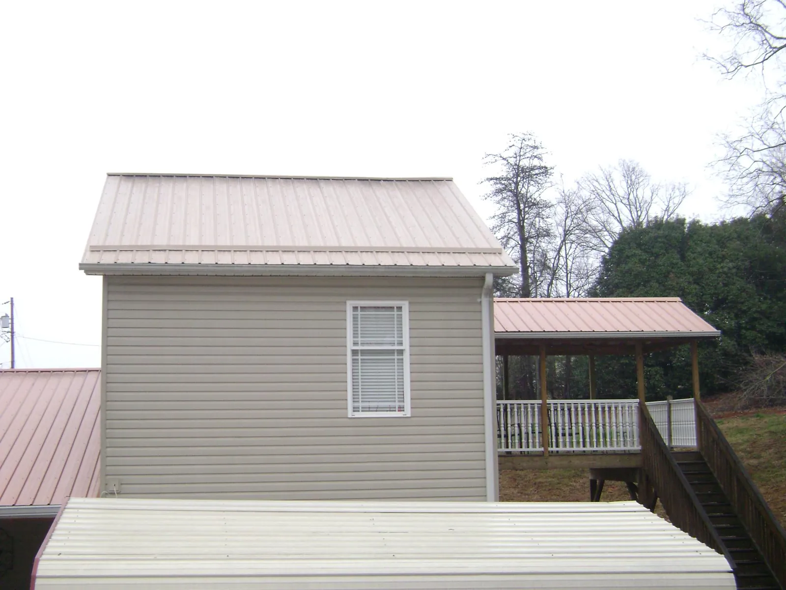 Tan metal roofs on a two story addition and attached porch, from a Roof Replacement job in Millville